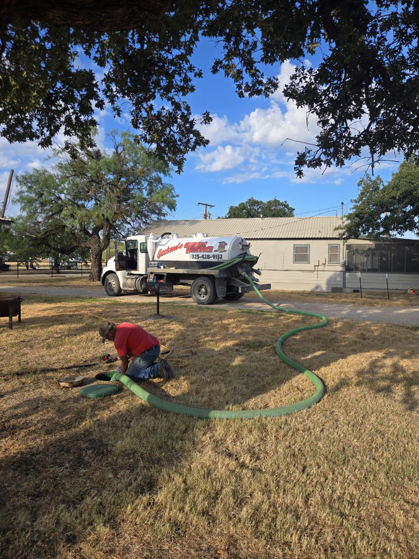 Technician kneeling at a septic lid with the service truck in the background