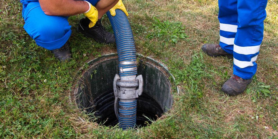 Two technicians servicing an open septic tank in a residential yard